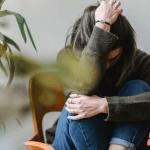 Anxiety, how can naturoapthy help with it? Lady sitting on a chair huddled, holding her head.